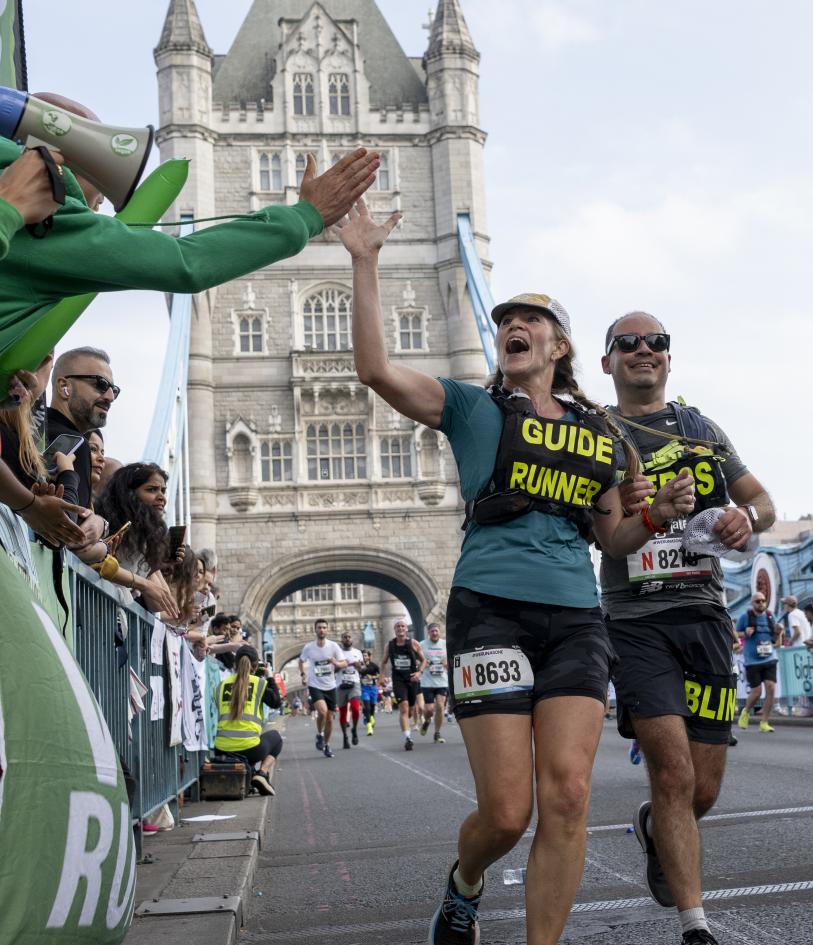 A guide runner high fives spectators on Tower Bridge