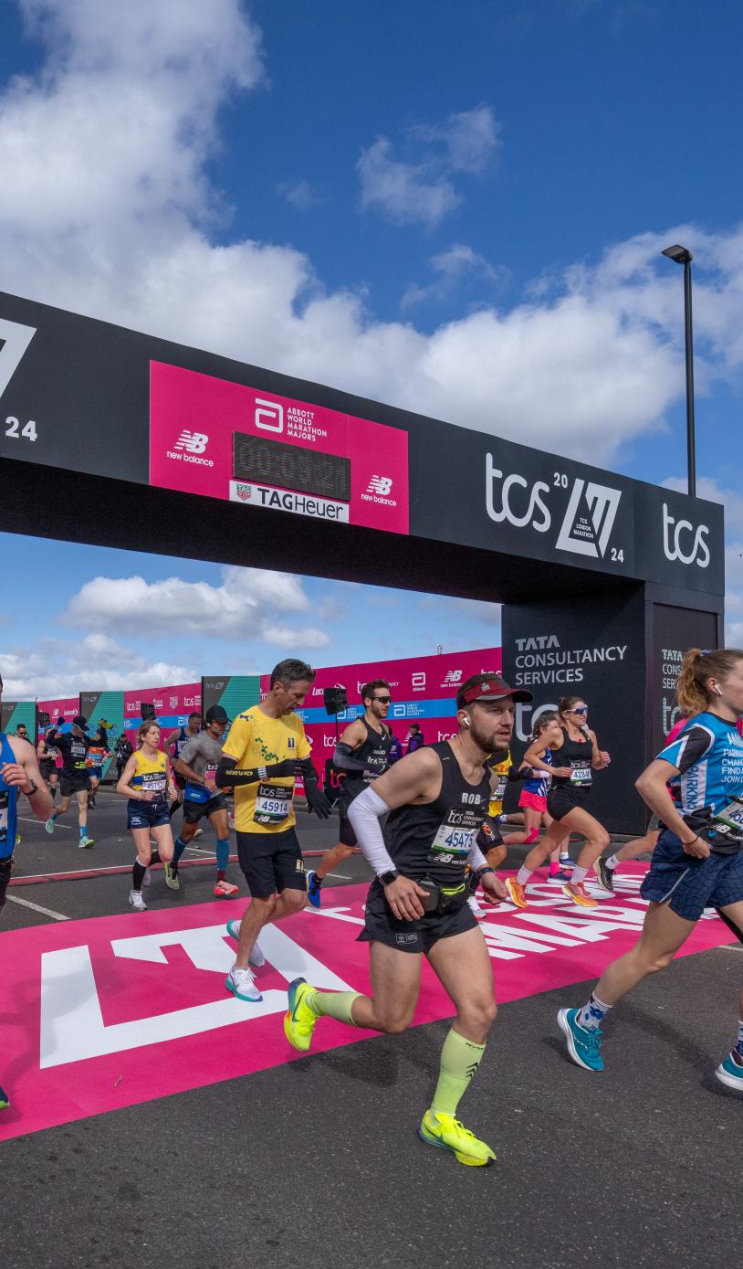 Multiple people running over the start line of the TCS London Marathon