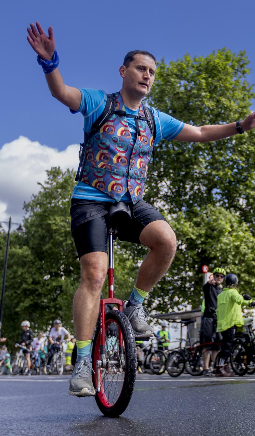 Man on unicycle by cycles past the London eye. 