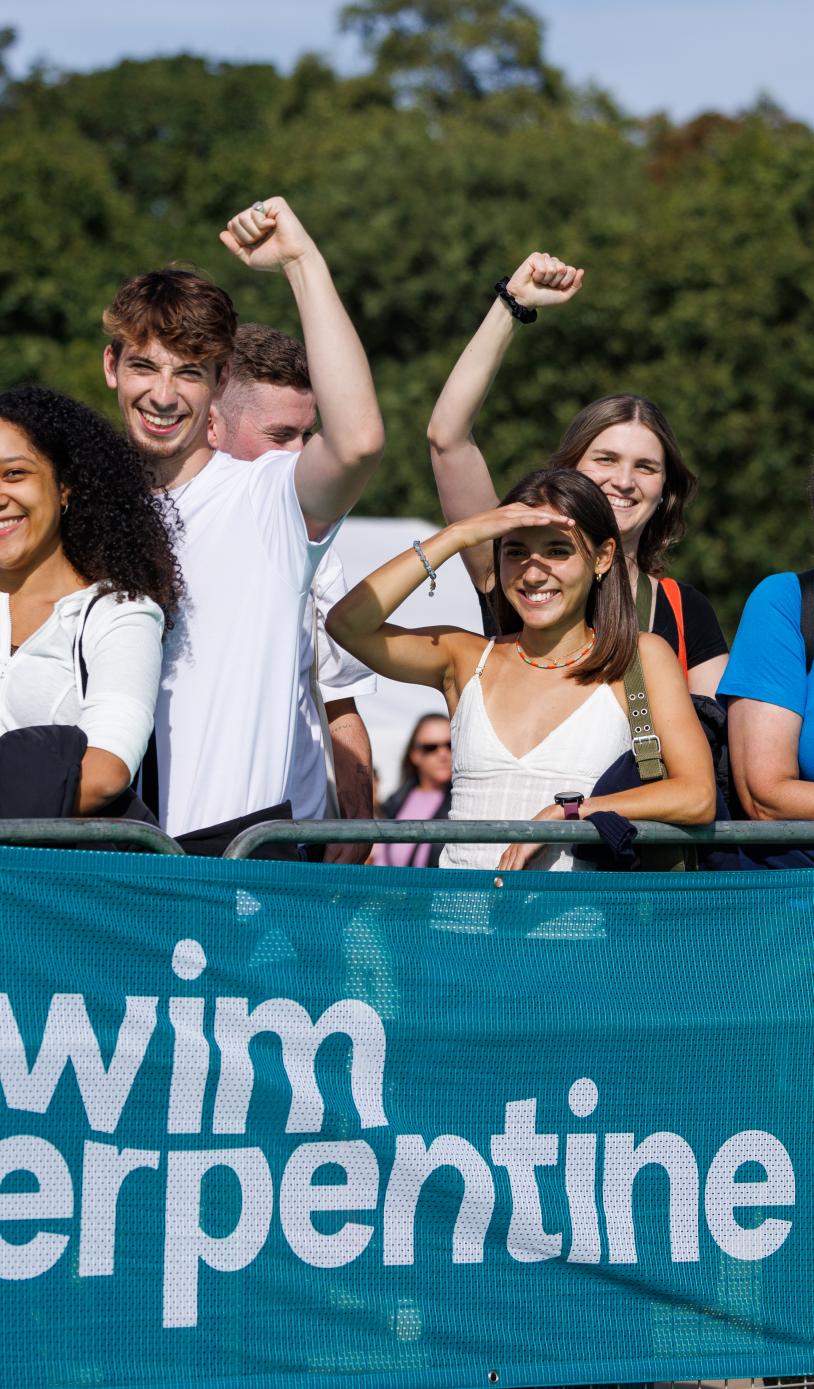 Group of people raise there hands in the air as they support the swimmers from behinde a barrier.