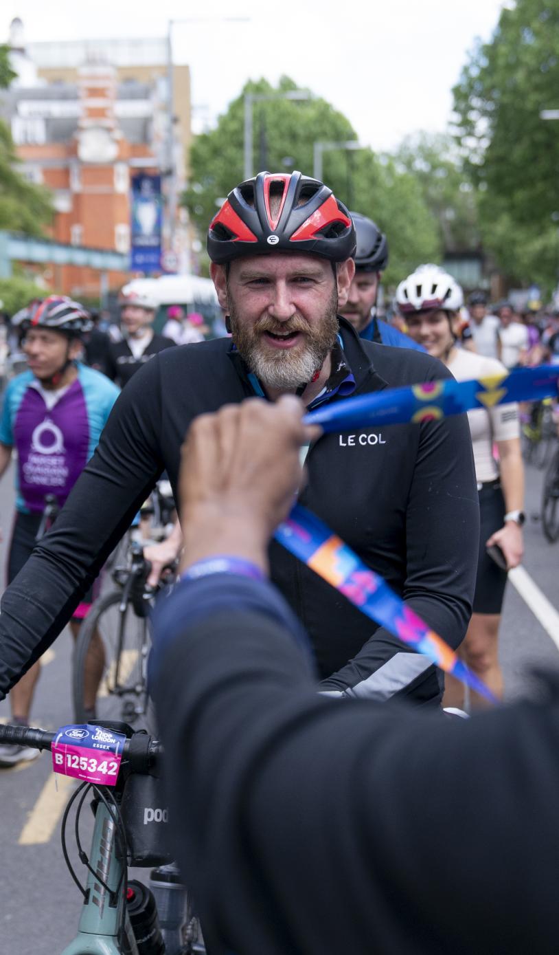 Volunteer holds out a medal to a cyclist finishing the RideLondon race.