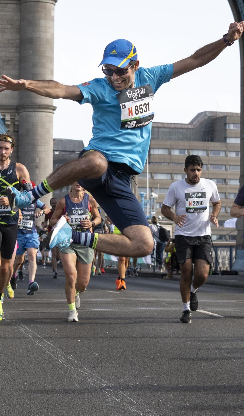 Man is jumping in the air clicking his heals on tower bridge as he competes in the big half.