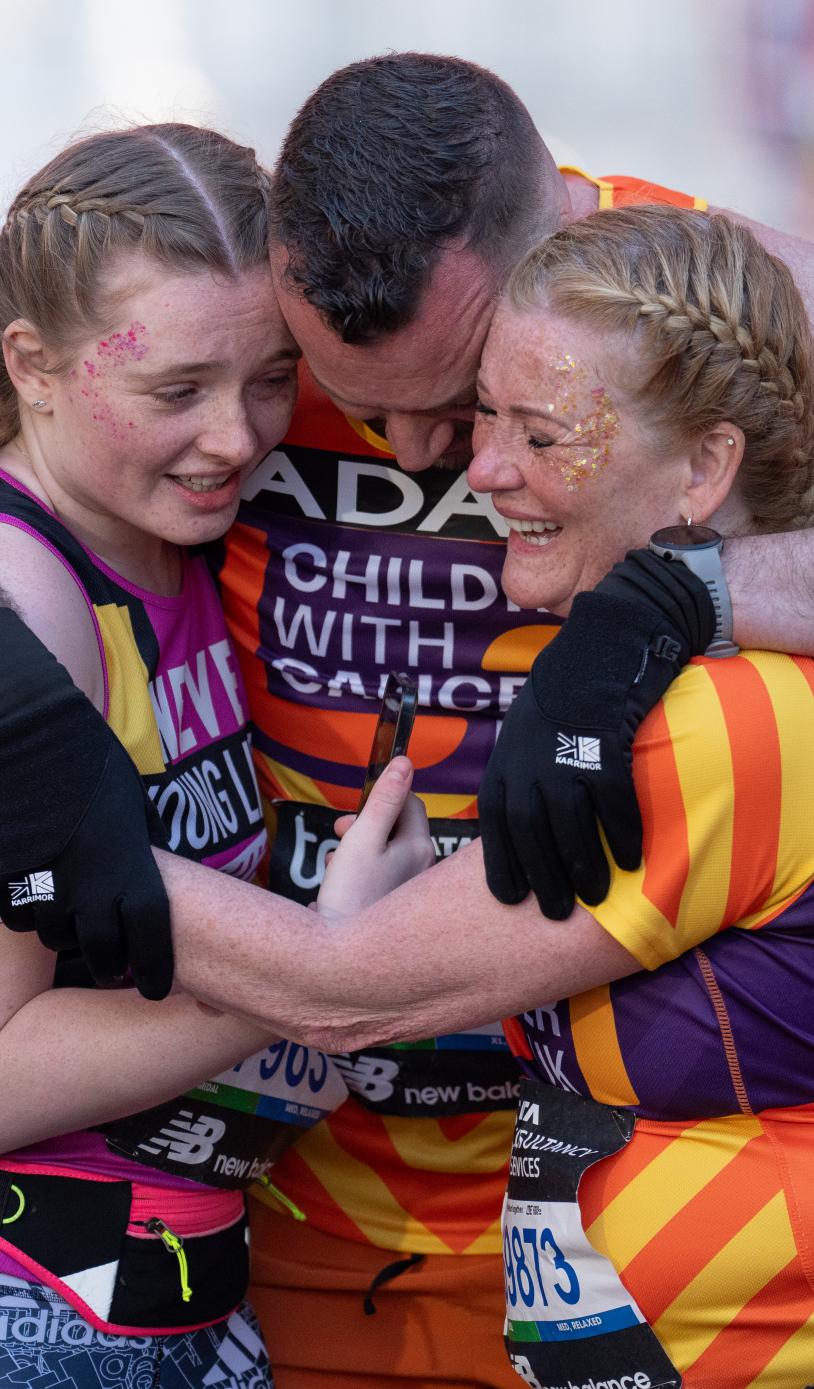 3 people embracing in a group hug wearing orange vests 