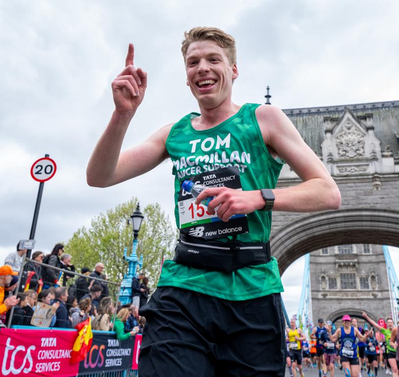 Runner in a green vest with a finger in the air celebrating. Tower bridge in the background. 