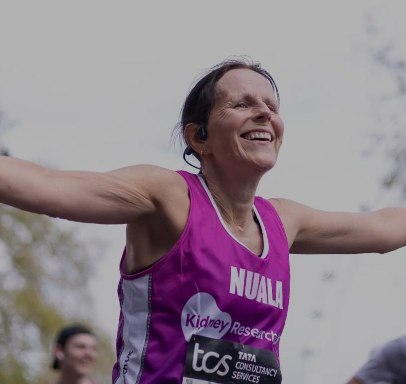 A runner with her arms out stretched in a charity running vest as she crosses the Finish Line