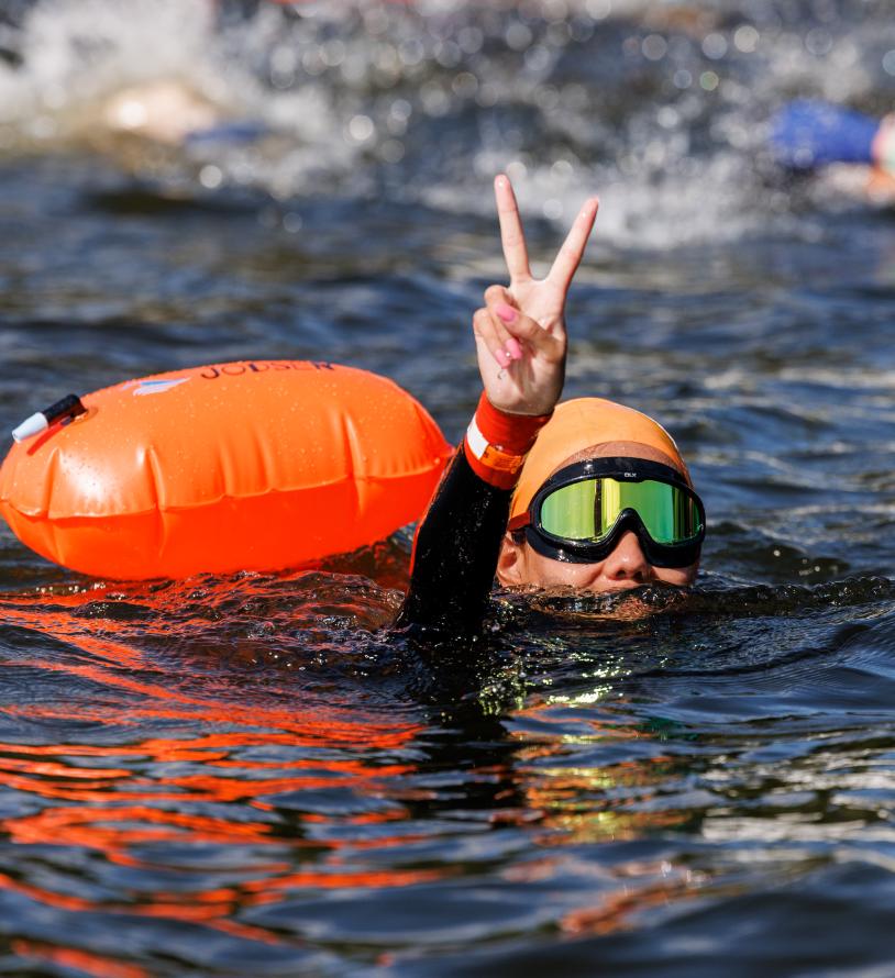 Swim Serpentine participant holds up a peace sign from the water